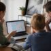 Gezin dat aan een vakantietafel reisopties vergelijkt op een laptop en reisgidsen bekijkt