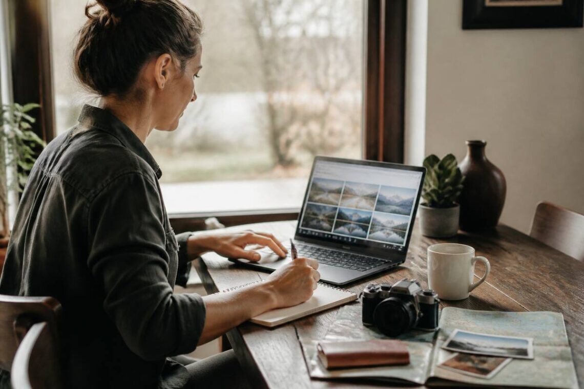 Iemand vergelijkt vakanties op laptop en noteert voorwaarden aan tafel